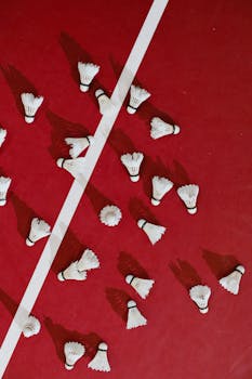 A top-down view of shuttlecocks scattered on a red badminton court.
