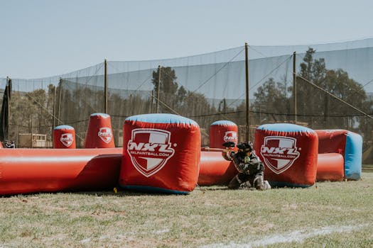 An action-packed paintball game outdoors with players in strategic positions behind inflatable barriers.