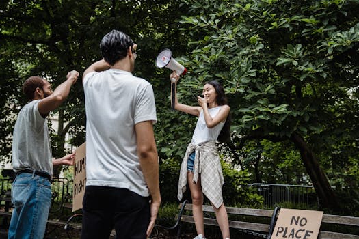 Group of people holding signs and a megaphone during a peaceful protest in a park setting.