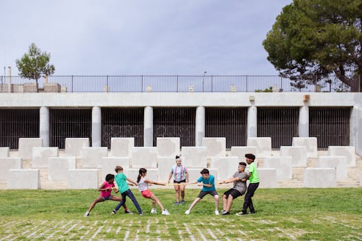 Kids enjoying a lively tug of war game outdoors in a park with a stone wall backdrop.